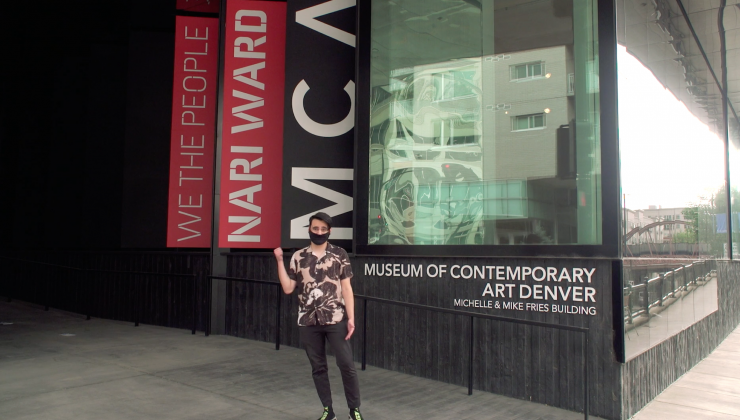 What to Expect on Your Visit to the Museum (A Video) Screenshot: Young man in a mask stands outside the museum and he stands in a printed shirt, black pants, and motions with his right hand to follow him.