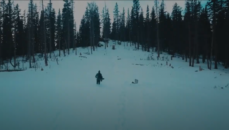 Screenshot of a man, at a distance, in the snow covered woods