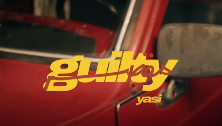 Screen grab image from a music video. The word “guilty” is printed in yellow and is overlaid on an image of a red truck. Underneath the word “guilty” is the musician's name—which is yasi—printed in the same font and color. 